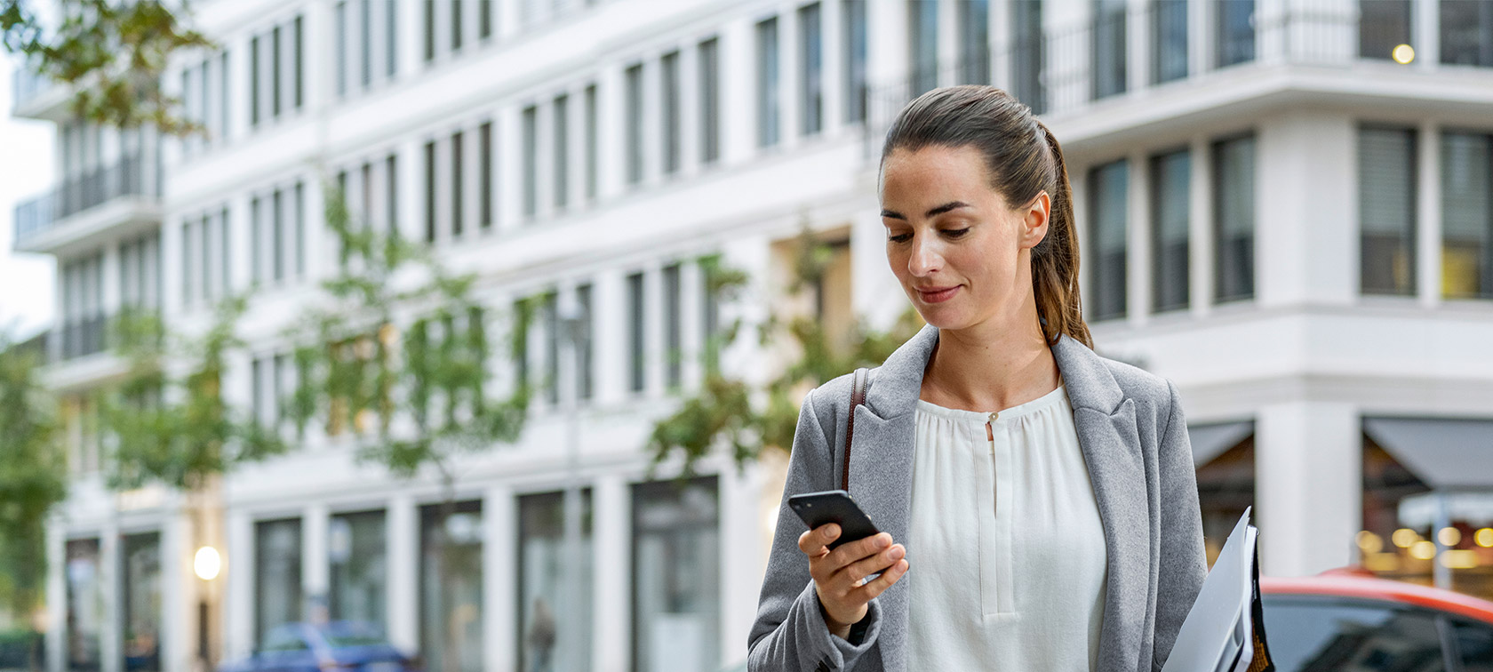 Remote Software Upgrade Frau steht vor Gebäude und schaut auf ihr Smartphone